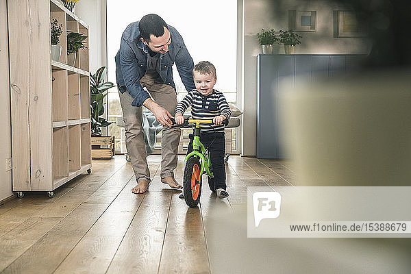 Father helping son riding with a balance bicycle at home