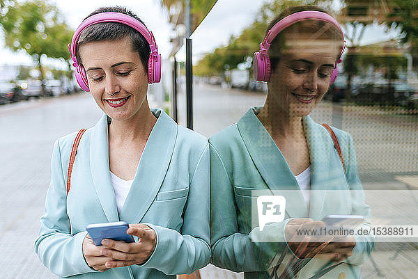 Frau in Jacke gekleidet  die mit ihrem Mobiltelefon Musik hört