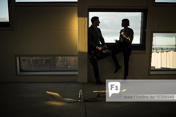 Colleagues sitting on window sill discussing after work