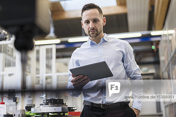 Geschäftsmann mit Tablette an einer Maschine in einer modernen Fabrik