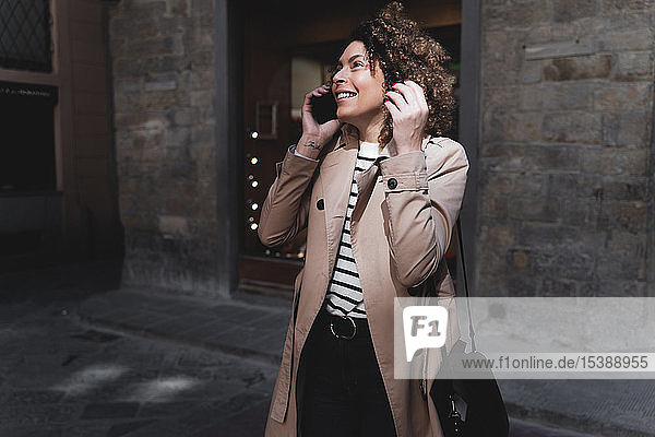Lächelnde Frau telefoniert mit Handy in einer Gasse