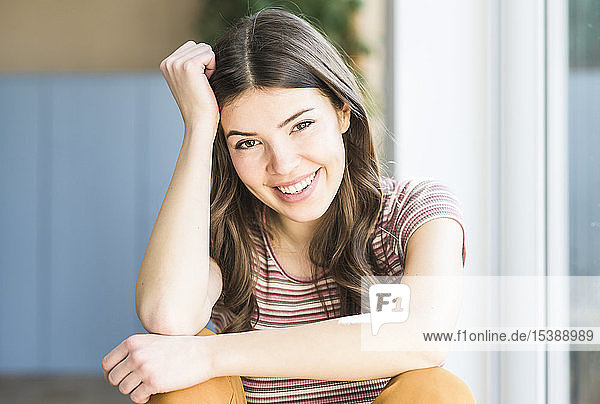 Porträt einer lächelnden jungen Frau  die zu Hause am Fenster sitzt