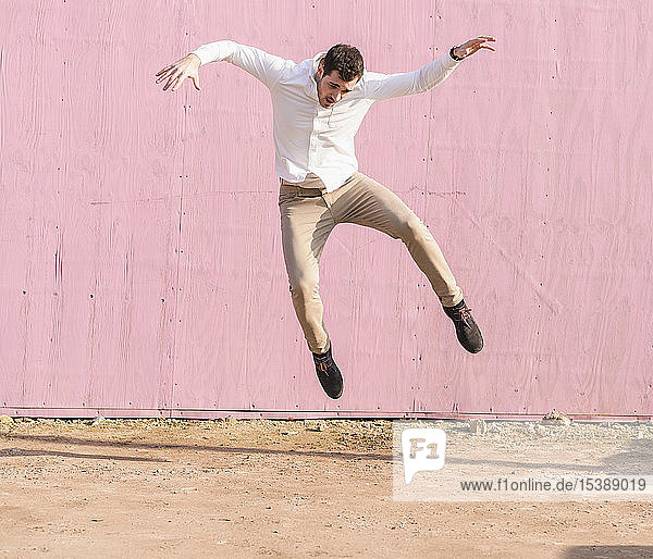 Überschwänglicher junger Mann springt vor rosa Wand