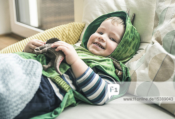 Happy boy in a costume lying down playing with toy figure at home