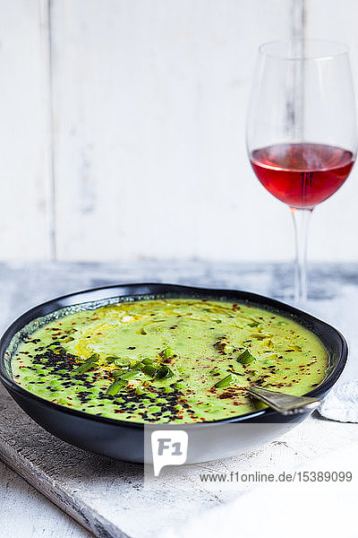 Schale mit frischer grüner Erbsensuppe mit Frühlingszwiebeln und einem Glas Rotwein