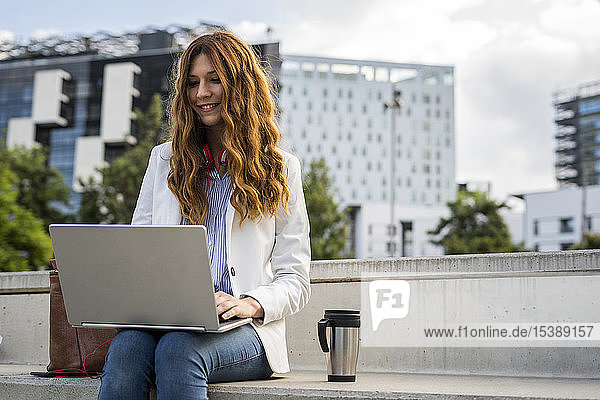 Junge Geschäftsfrau sitzt auf einer Treppe in der Stadt und arbeitet mit einem Laptop