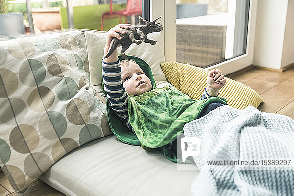 Boy in a costume lying on amattress playing with toy figure at home
