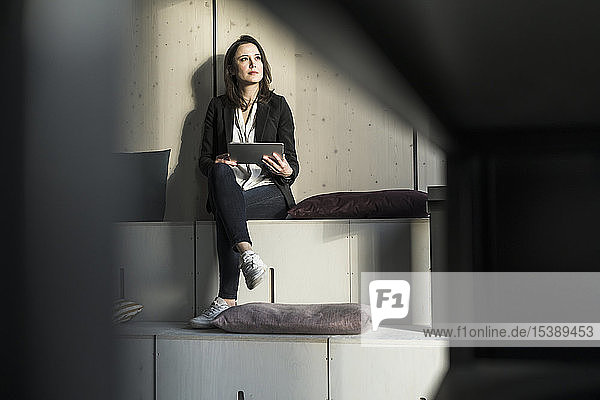 Businesswoman with tablet sitting in lounge area in office