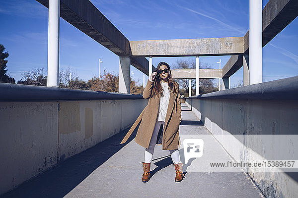 Young woman wearing coat and sunglasses standing on a bridge
