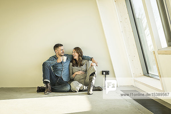 glückliches Paar  ein Baby erwartend  auf dem Boden ihrer neuen Wohnung sitzend