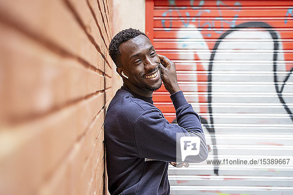 Porträt eines glücklichen jungen Mannes  der mit drahtlosen Kopfhörern und Smartphone Musik hört
