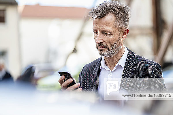 Porträt eines reifen Geschäftsmannes beim Blick auf das Handy