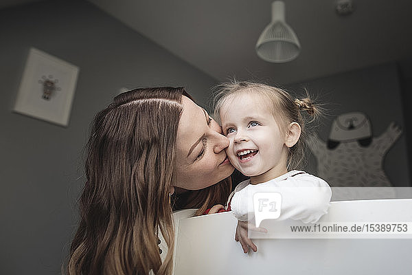 Mother kissing happy daughter in children's room