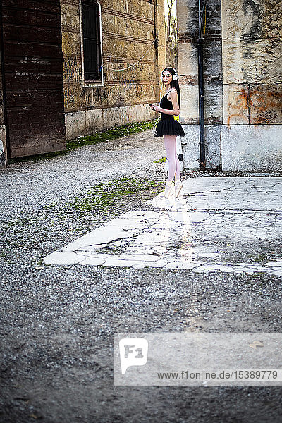 Italy  Verona  woman in ballet dress with cell phone and headphones standing at an old building