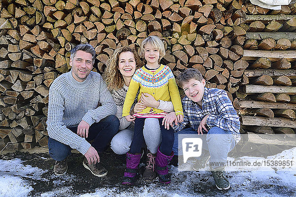 Portrait of happy family in front of stack of wood in winter