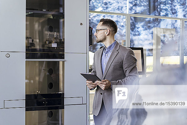 Businessman with tablet looking at machine in a modern factory