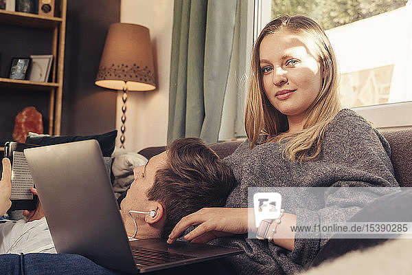 Young couple relaxing on sofa and using notebook  smartphone and ebook reader