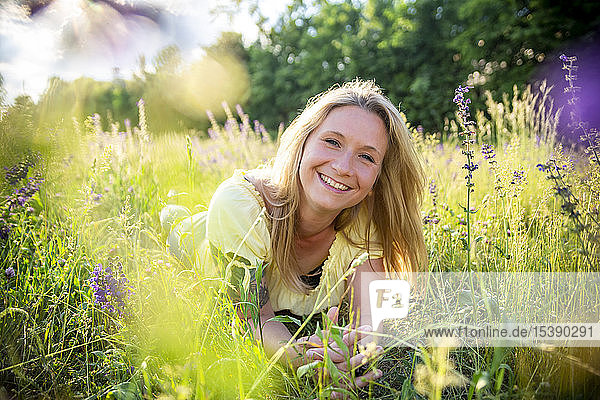 Portrait of happy blond woman lying on flower meadow in summer