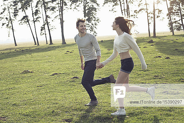Happy young couple running hand in hand on meadow
