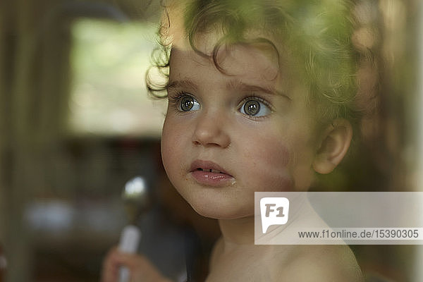 Porträt eines kleinen Mädchens hinter einer Fensterscheibe beim Essen