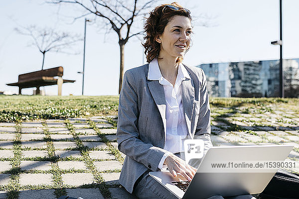 Geschäftsfrau in der Stadt  am Boden sitzend  am Laptop arbeitend