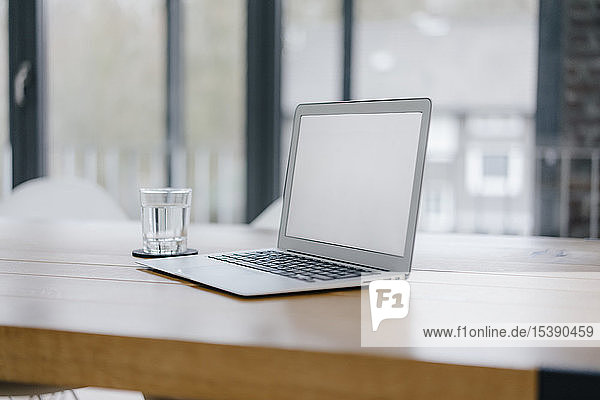 Laptop auf dem Schreibtisch im Büro mit einem Glas Wasser
