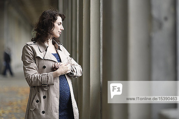 Profil einer schwangeren Frau im Trenchcoat an der Kolonnade