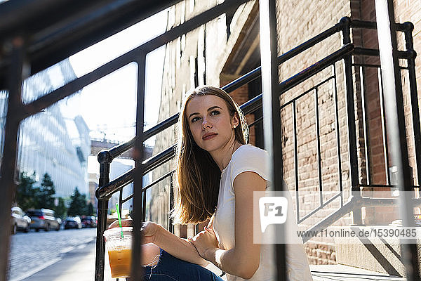 Junge Frau erkundet New York City  sitzt auf einer Treppe und trinkt Kaffee
