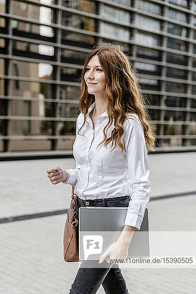 Young businesswoman walking in the city  carrying laptop