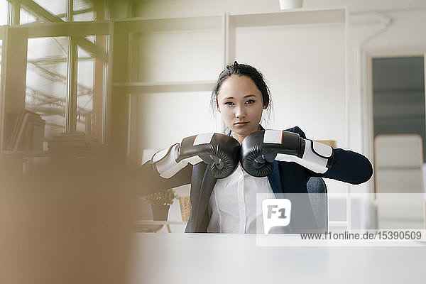 Portrait of young businesswoman sitting at desk wearing boxing gloves