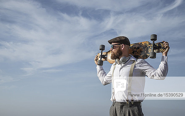 Bearded man with longboard on his shoulders looking at distance