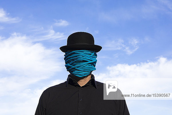 Man wearing bowler hat with rope wrapped around his face
