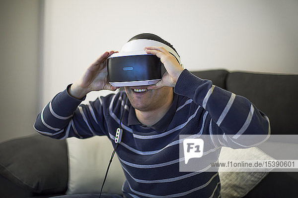 Laughing young man on couch at home using VR glasses