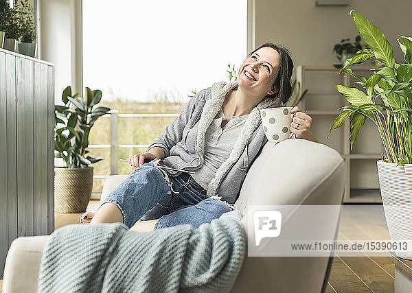 Glückliche Frau mit Becher und Tablette  die zu Hause auf der Couch sitzt