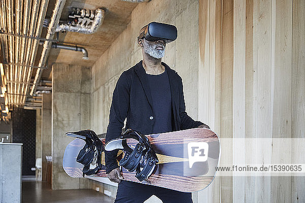 Reifer Geschäftsmann mit VR-Brille und Snowboard in modernem Büro