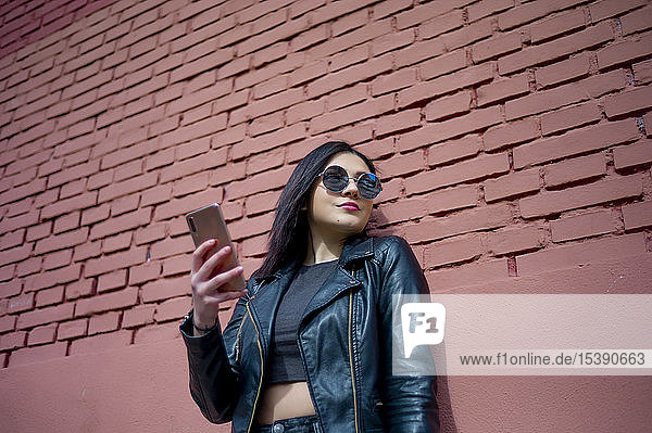 Portrait of young woman with smartphone wearing sunglasses and black leather jacket
