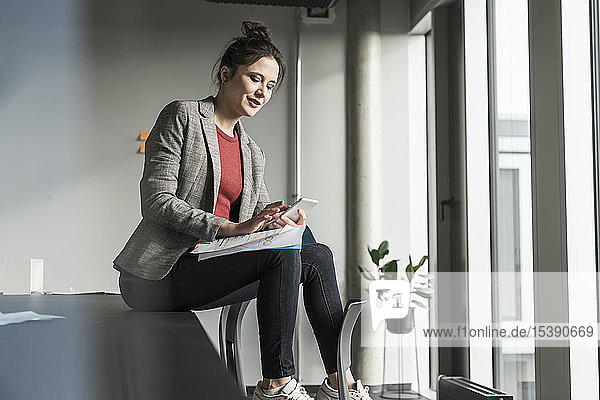 Businesswoman sitting on desk in office using cell phone