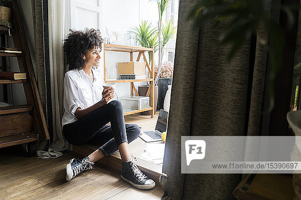 Relaxed woman sitting on floor of her flat  drinking coffee