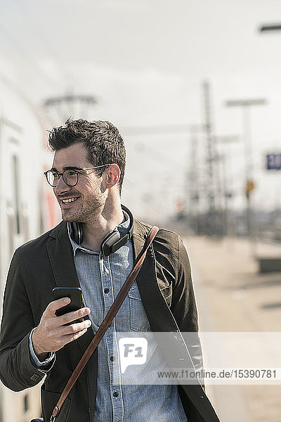Smiling young man with cell phone at station platform