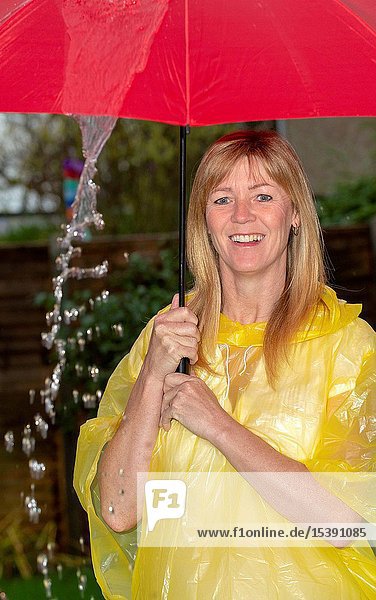 Woman wearing a yellow poncho holding a red umbrella in the rain