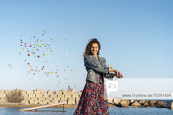Porträt einer lächelnden jungen Frau  die Konfetti in die Luft wirft