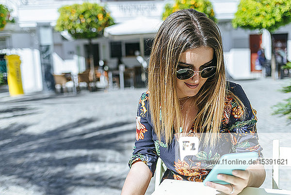 Spanien  Cádiz  Vejer de la Frontera  junge Frau sitzt im Straßencafé und schaut auf ihr Handy