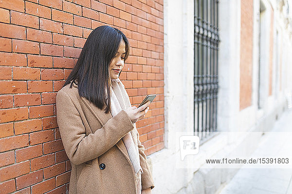 Junge Frau benutzt Handy an Ziegelmauer
