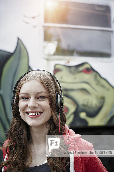 Portrait of happy teenage girl wearing headphones at a painted train car