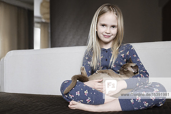 Portrait of smiling little girl wearing pyjama with floral design holding cat in her arms
