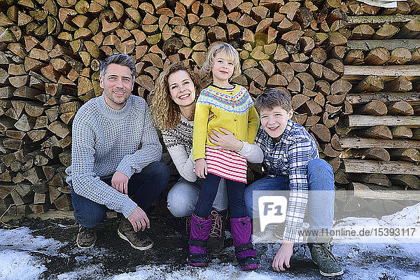 Porträt einer glücklichen Familie vor einem Holzstapel im Winter