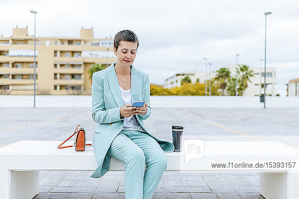 Frau in Anzugsjacke sitzt auf Bank und benutzt Mobiltelefon