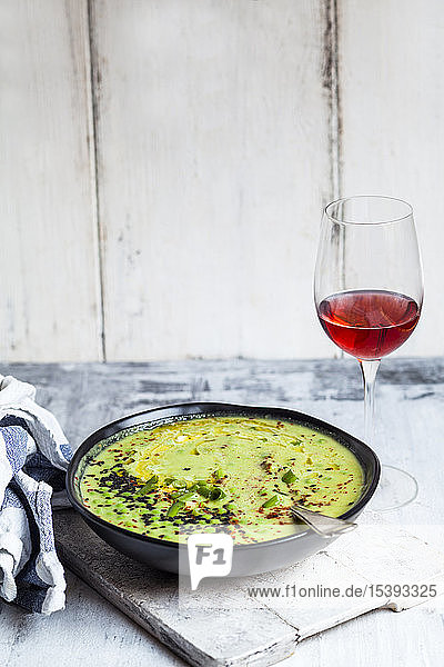 Schale mit frischer grüner Erbsensuppe mit Frühlingszwiebeln und einem Glas Rotwein