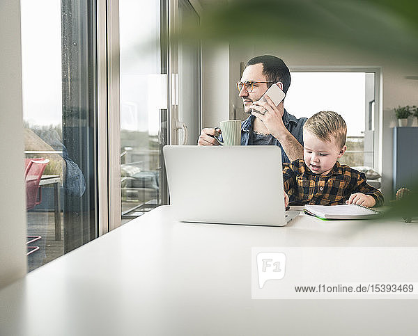 Father working at table in home office with son sitting on his lap