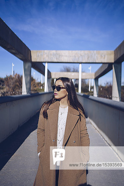 Young woman wearing coat and sunglasses standing on a bridge